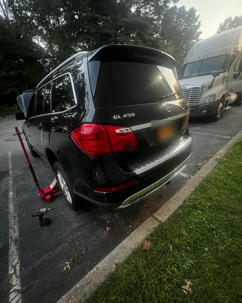 Black Mercedes GL450 lifted on a red floor jack in a parking lot during a road call